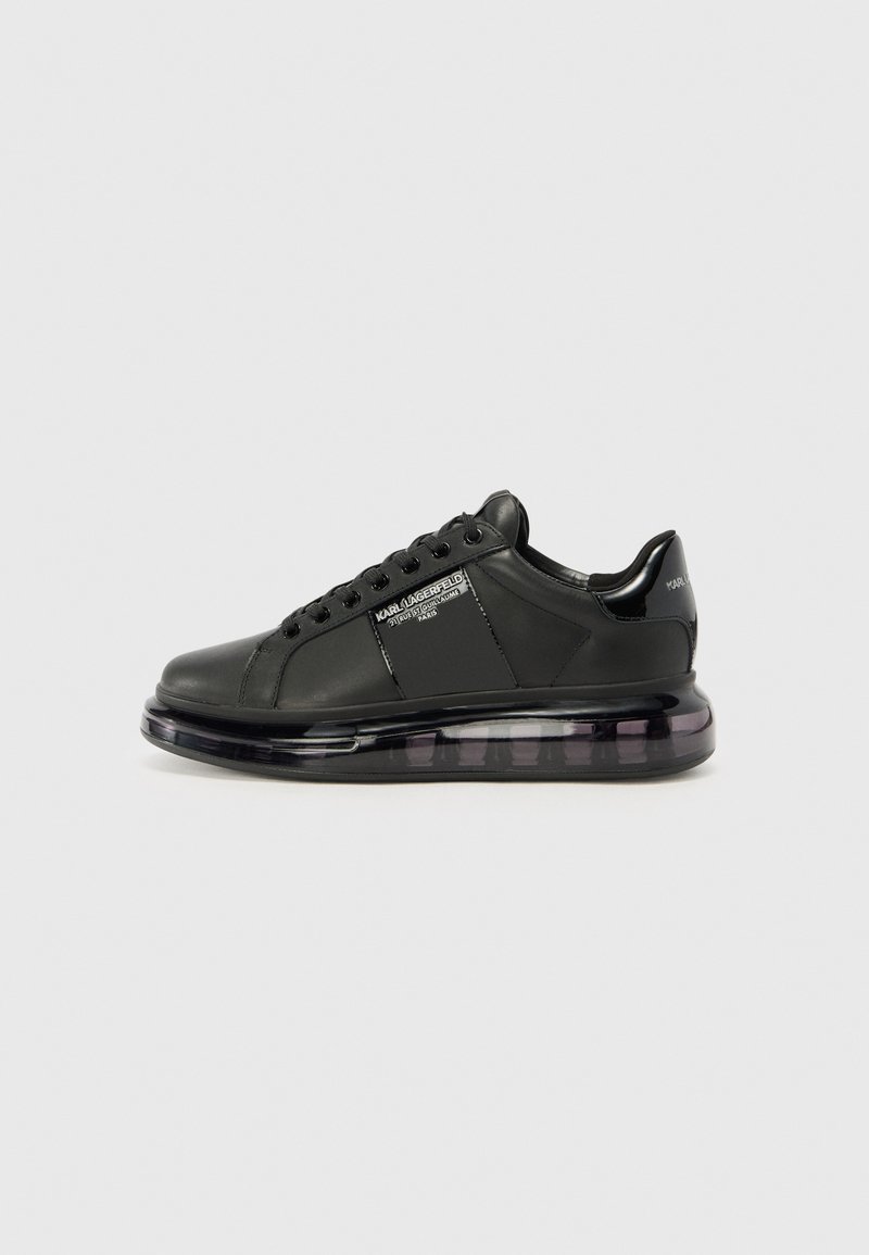 Sneaker nera con tomaia in pelle liscia, punta rotonda e design con lacci. Presenta una suola trasparente e ammortizzata con un gradiente scuro.