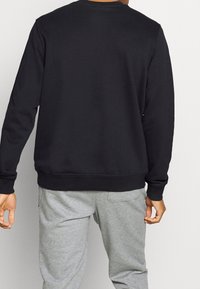 Czarna bluza z długimi rękawami, z ribbowanymi mankietami i dołem, wykonana z miękkiego materiału. Noszona z szarymi dresami, prezentującymi luźny krój.