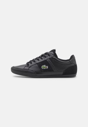 Sort lavtop sneaker med snøredesign, teksturerede paneler og en grøn krokodille-logo på siden.