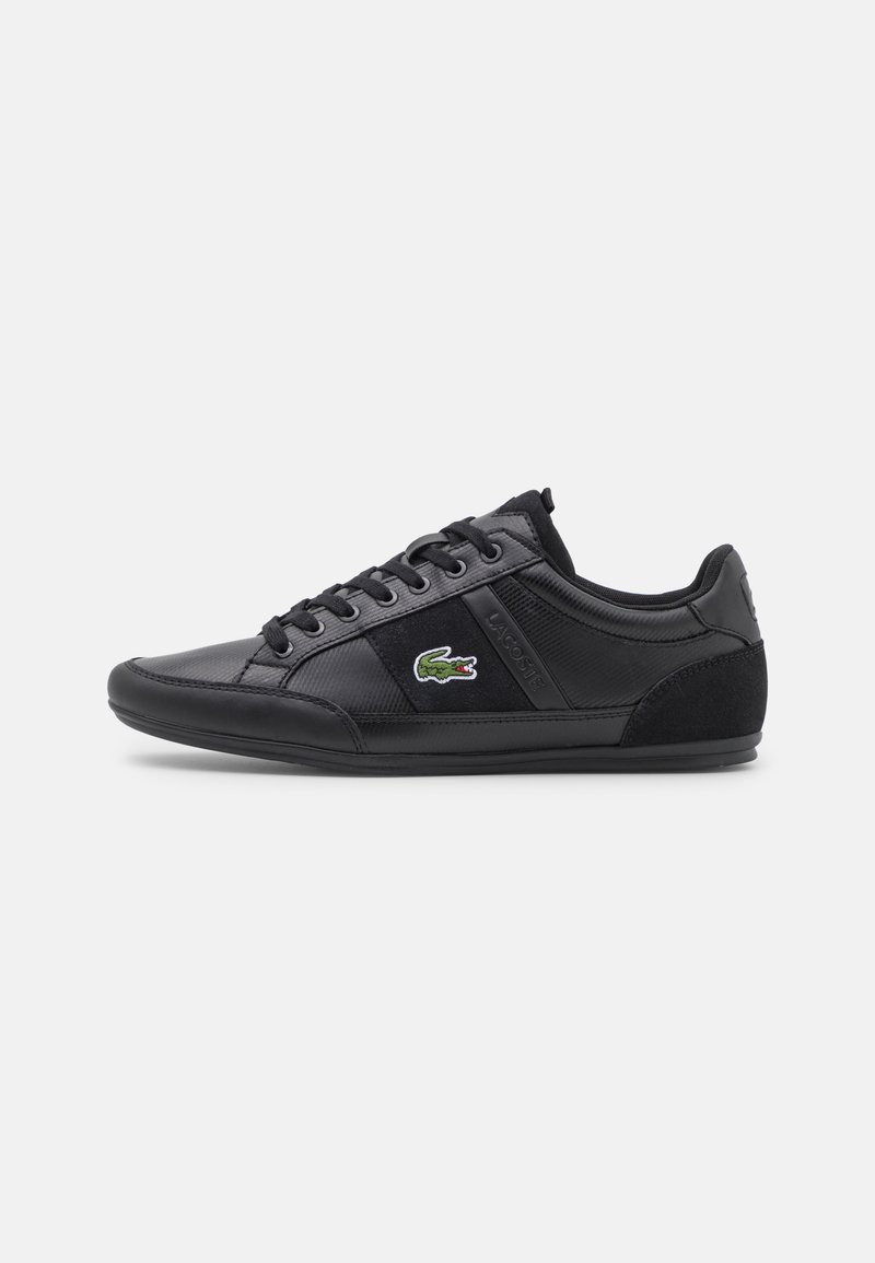 Baskets basses noires avec lacets, panneaux texturés et logo crocodile vert sur le côté.