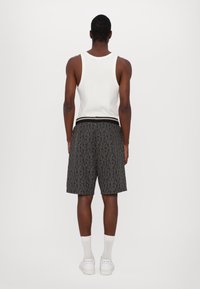 Pantalones cortos negros con un patrón geométrico, cintura elástica y camiseta sin mangas blanca. La modelo lleva calcetines blancos y zapatillas. Vista trasera.