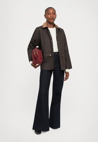 Brown jacket with a tan collar, white sweater underneath, paired with dark flared jeans and a burgundy handbag. Gold hardware accents.