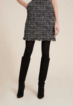 Mini falda de tejido en blanco y negro con borde de flecos, combinada con botas negras de ante hasta la rodilla. Textura suave y diseño estructurado.