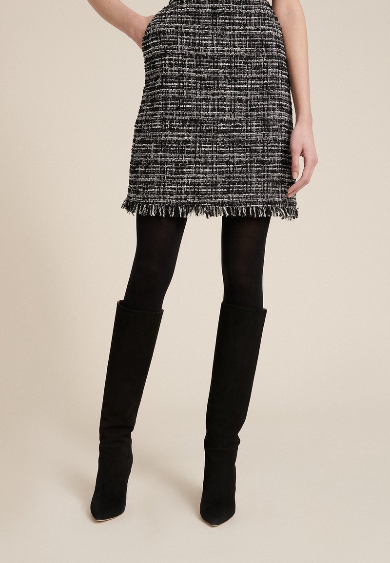 Svartvit vävd minikjol med franskant, matchad med knähöga svarta mockastövlar. Slät textur och strukturerad design.