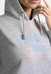 Pilkas džemperis su kapuce ir raišteliu, ant kurio užrašyta šviesiai mėlyna spalva "LONGSD" ir liūto grafika. Minkšta medžiaga, o kapučė suteikia šilumos.