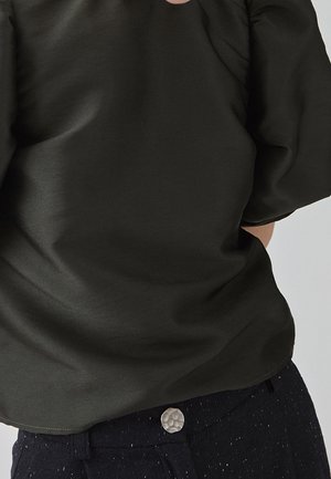 Donkergroen, kortermig shirt met een gladde textuur en lichte plooien bij de schouders, gecombineerd met een donkere broek met een gestructureerde knoop.