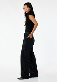 Body negro con mangas de campana combinado con jeans negros de pierna ancha que presentan un ligero brillo y bolsillos laterales, todo ello sobre un fondo blanco.