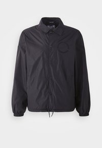 Black lightweight jacket with a button-up front, elastic cuffs, drawstring hem, and embroidered logo at chest. Smooth, slightly shiny fabric.