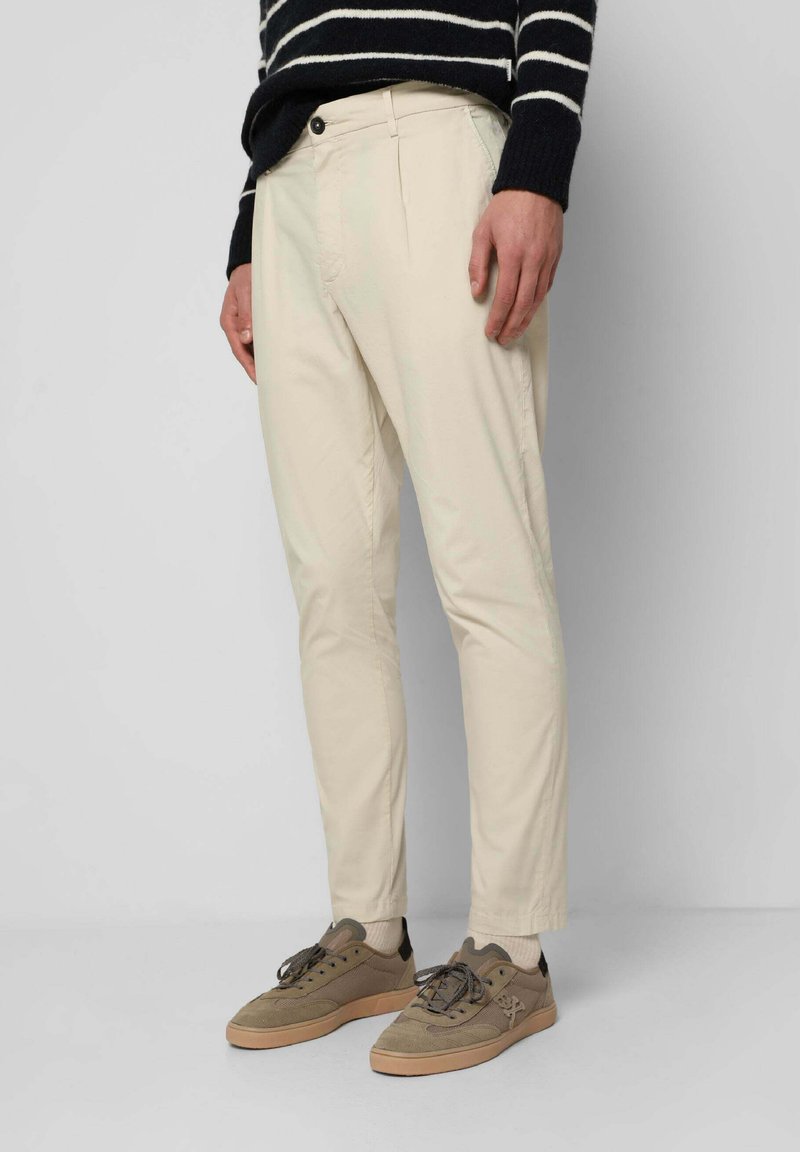 Chinos beige de corte slim, con cremallera, bolsillos delanteros y una textura suave. Combinados con zapatillas marrones para un look casual.