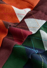 Knit fabric featuring a diamond pattern in orange, dark burgundy, white, and green, accented with contrasting colored stitching lines.