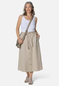 Beige Leinenrock mit Bindeband in der Taille, Frontknöpfen und Seitentaschen, getragen mit einem weißen Tanktop und beigen Sneakers sowie einer Umhängetasche.