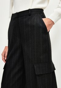 Schwarze, gestreifte Hose aus strukturiertem Stoff, mit einem Bund, seitlichen Taschen und einer Cargotasche am Bein.