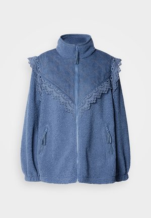 Sinine fliisjakker kõrge kaelusega, millel on kontrastne tikitud denimpaneel ja pitsäär. Sisaldab lukuga küljetaskuid.