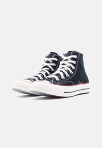 Ψηλά αθλητικά παπούτσια από ναυτικό μπλε καμβά με λευκά κορδόνια, λαστιχένια σόλα και κόκκινες λεπτομέρειες. Διαθέτουν ραφές και λογότυπο "love" στην πλευρά.