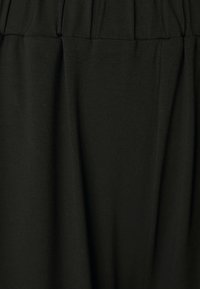 Svart tyg med en slät yta och mjuk fall. Har samlat detaljer vid midjan och en flödande silhuett.