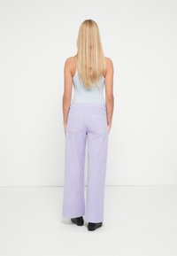 Pantalones de pierna ancha en tono lila claro, confeccionados en tela texturizada, con bolsillos traseros y cintura elástica, combinados con una camiseta ajustada azul.