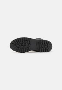 Suela de bota de goma negra con patrón de huella profunda y superficie texturizada. Presenta el logo de la marca en el costado y un diseño de puntas redondeadas.