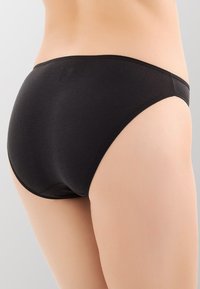 Mutande in cotone nero in stile bikini, con un design senza cuciture, morbida al tatto e con un cinturino a vita bassa. Minimalista e di colore uniforme.