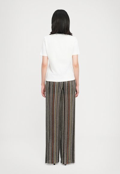 T-shirt blanc à manches courtes associé à un pantalon large à rayures noires et multicolores, avec des motifs verticaux et une coupe décontractée.