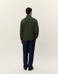 Maglione in pile verde con colletto alto, vestibilità rilassata. Abbinato a pantaloni blu navy, con una texture liscia e un design pulito.