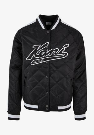 Svart vadderad bomberjacka med vitt randigt krage och manschetter, har en stor broderad "Kani"-logotyp och tryckknappsstängning.