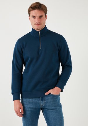 Navy blue fleece sweatshirt with a high collar, half-zip closure, long sleeves, and ribbed cuffs. Smooth texture and relaxed fit.