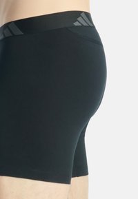 Zwarte sportshorts met een gladde textuur en een brede elastische tailleband met subtiele logo-accenten aan de voorkant.