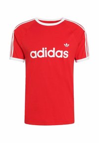 Červené bavlnené tričko s bielymi doplnkami a tromi bielymi pruhmi na rukávoch. S veľkým bielym logom "adidas" na prednej strane. Štandardný strih.