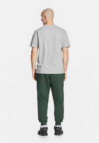 Szara bawełniana koszulka z krótkim rękawem w połączeniu z zielonymi dresami z elastycznymi mankietami, noszona z czarnymi butami sportowymi.