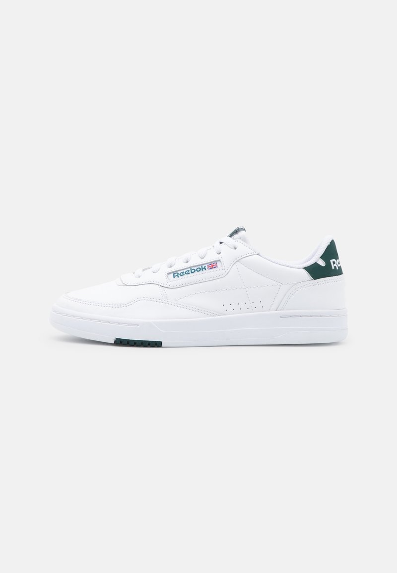 Baskets basses blanches Reebok avec languette de talon verte, fermeture à lacets, et logo Reebok avec l'Union Jack sur le panneau latéral.