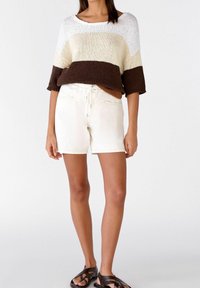 Suéter de punto con rayas en crema, marrón y óxido; combinado con pantalones cortos blancos que tienen una cinturilla con cordón y dos bolsillos delanteros. Sandalias negras.