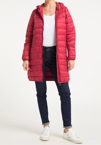 Rode pufferjas met een capuchon, voorzien van een ritssluiting aan de voorkant, zijzakken, een doorgestikte textuur en lange mouwen, gecombineerd met donkere jeans en witte sneakers.