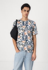 Tricou cu imprimeu floral, prezentând frunze tropicale și flori roz, asortat cu blugi evazați de culoare albastru deschis și o geantă neagră tip sling.