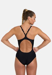 Maillot de bain une pièce noir avec bretelles réglables, design dos nu et texture lisse. Présente une jambe haute pour un confort de mouvement.