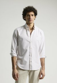 Camisa abotonada de color claro con mangas largas, puños doblados y un pequeño logotipo bordado. Hecha de una tela suave con un diseño clásico.