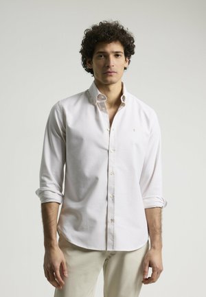 Camisa abotonada de color claro con mangas largas, puños doblados y un pequeño logotipo bordado. Hecha de una tela suave con un diseño clásico.