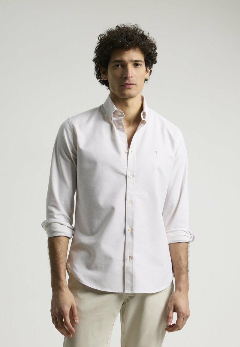 Camisa abotonada de color claro con mangas largas, puños doblados y un pequeño logotipo bordado. Hecha de una tela suave con un diseño clásico.