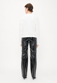 Weißer Pullover mit Rundhalsausschnitt, kombiniert mit glänzenden schwarzen High-Waist-Hosen. Beide Kleidungsstücke weisen einen lässigen Schnitt und glatte Texturen auf.