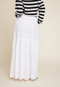 Hvit maxi skjørt med lagdelte volanger, laget av lett materiale. Stylet med en svart og hvit stripete genser, som har en elastisk midje.