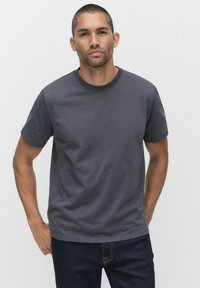 Mørkegrå bomulds T-shirt med korte ærmer, rund halsudskæring og en glat tekstur. Sammen med mørkeblå jeans, stående mod en neutral baggrund.