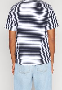 Man wearing a navy and white horizontal striped short-sleeve shirt with light blue denim jeans, shown from the back.