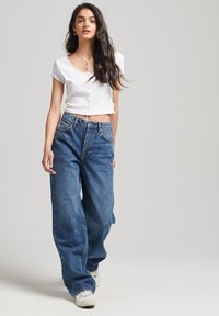 Top corto de manga corta blanca con botones, combinado con jeans de denim azul sueltos, con cintura alta y corte wide-leg. Zapatillas blancas.