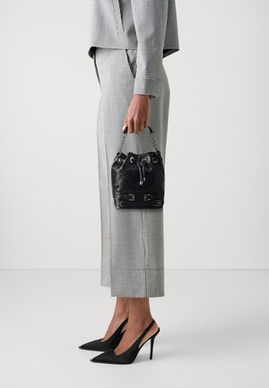 Sac d'ordinateur en cuir noir avec une fermeture à cordon, une anse en chaîne et des accents métalliques, assorti à une tenue à carreaux et des talons pointus.