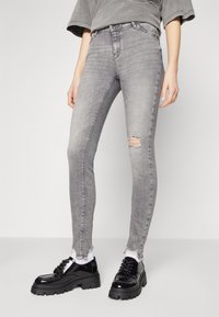 Jeans ajustados grises con detalles desgastados en las rodillas, combinados con zapatos negros gruesos. Los jeans tienen una cintura de tiro bajo y una textura apagada.