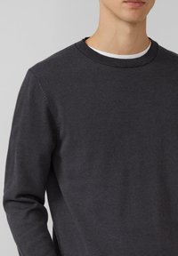 Ciemnoszary sweter z okrągłym dekoltem o delikatnej prążkowanej strukturze, kontrastującym jasnym wewnętrznym kołnierzem i dopasowanymi długimi rękawami.