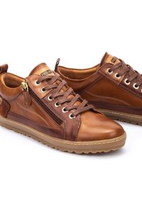 Zapatos de cuero marrón con un acabado texturizado, que presentan un cierre zipper, un diseño con cordones y una suela de goma. Destacan los acentos de ferretería en color dorado.