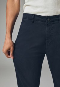 Pantaloni blu navy realizzati in tessuto di cotone, dotati di una vita standard, tasche frontali e una finitura liscia e lavorata.