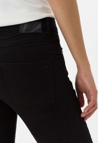 Jeans negros con una cinturilla texturizada, que cuentan con un bolsillo trasero y un diseño ajustado. Tejido suave con detalles de costura.