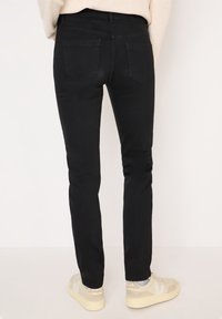 Jeans skinny neri con una texture liscia. Dotati di due tasche posteriori e vita a media altezza. Abbinati a sneakers beige chiaro.