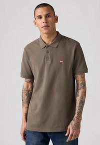 Bruine poloshirt in een katoenmix, met een klassieke kraag, drie knoppen en een rood Levi's logo op de linkerborst. Eenvoudig ontwerp.